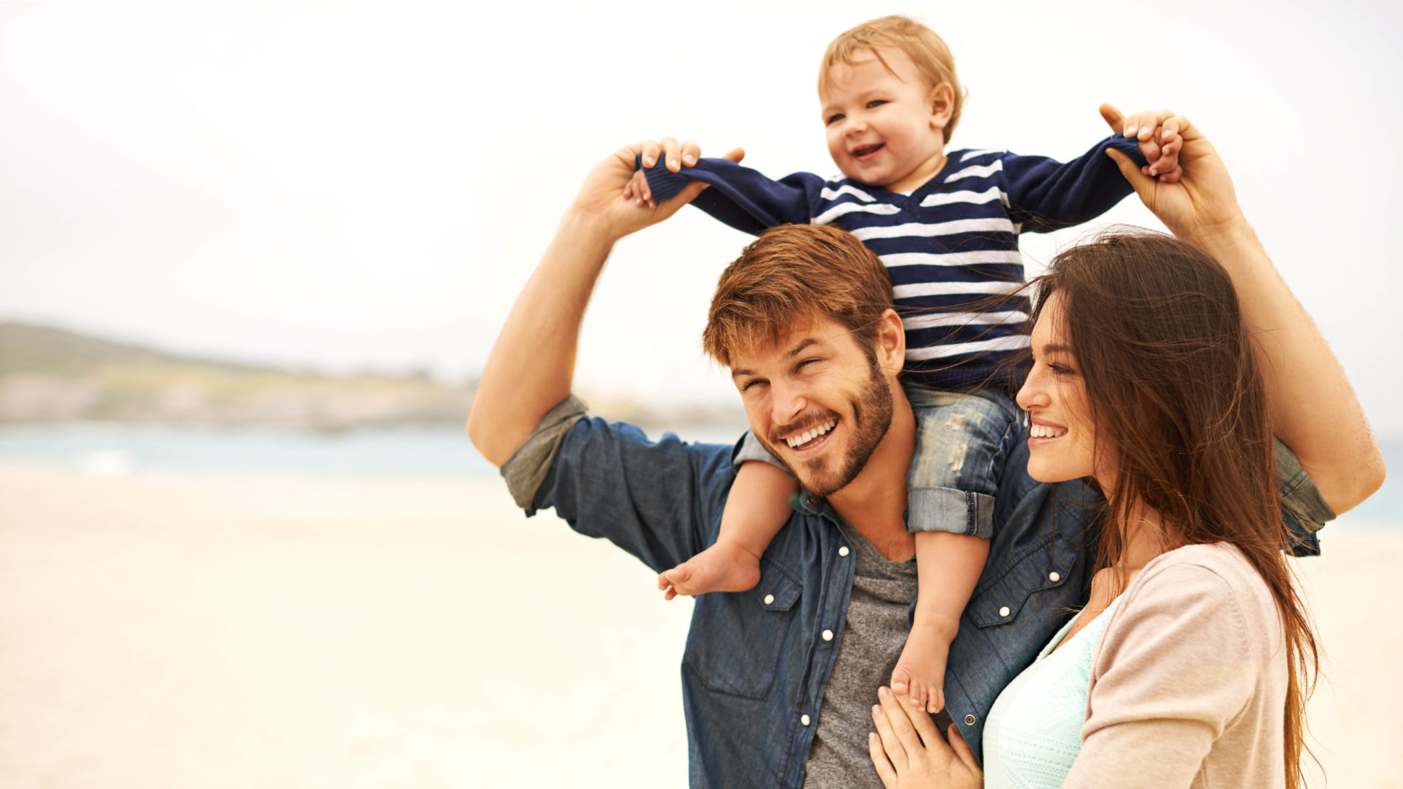 Daddy carrying his son on shoulders along with mom near sea shore